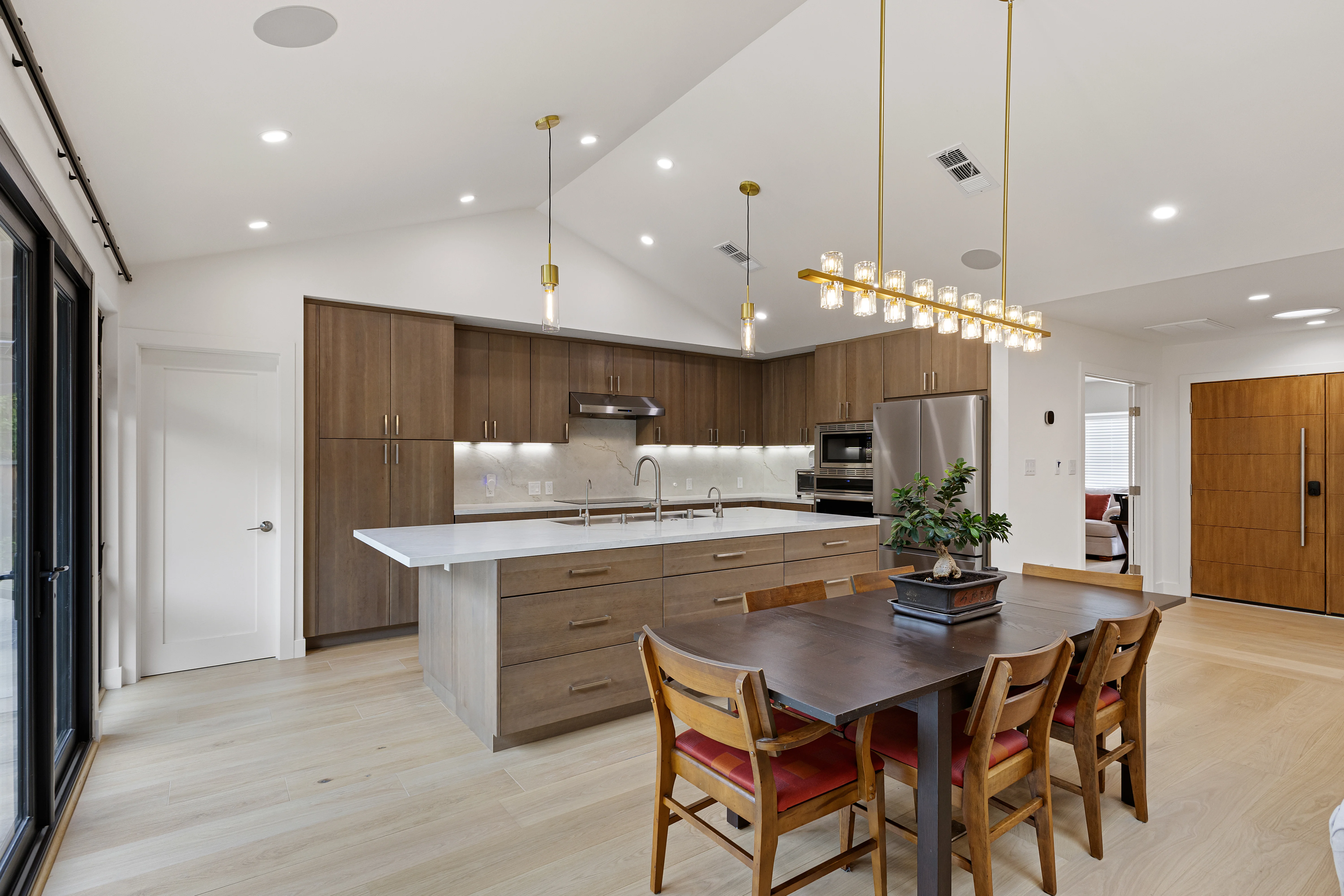 Modern kitchen with walnut flat-panel cabinetry, waterfall island and brass pendant lights over dining table