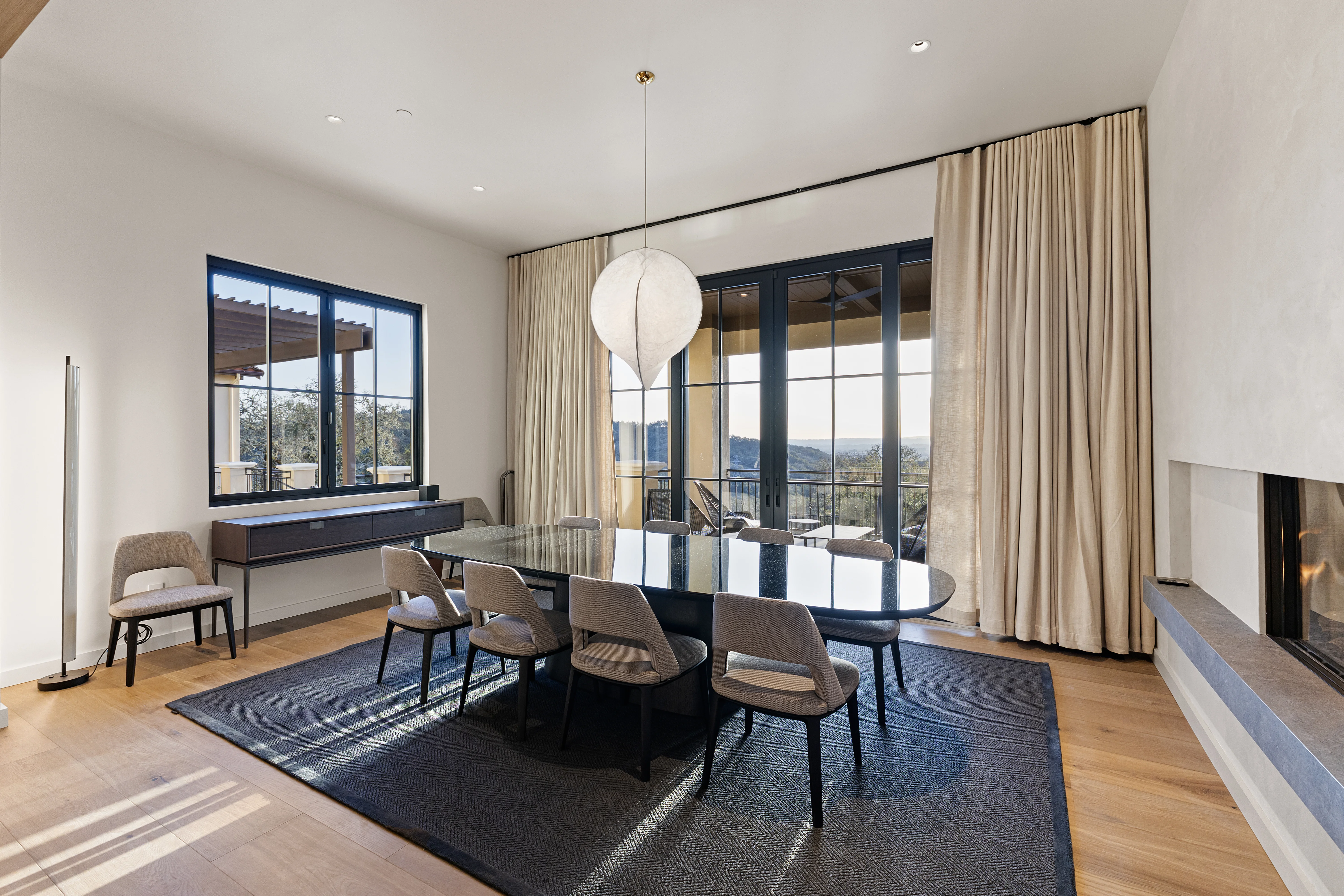 Elegant dining room with hill views, floor-to-ceiling glass doors, linen drapes and a sculptural globe pendant