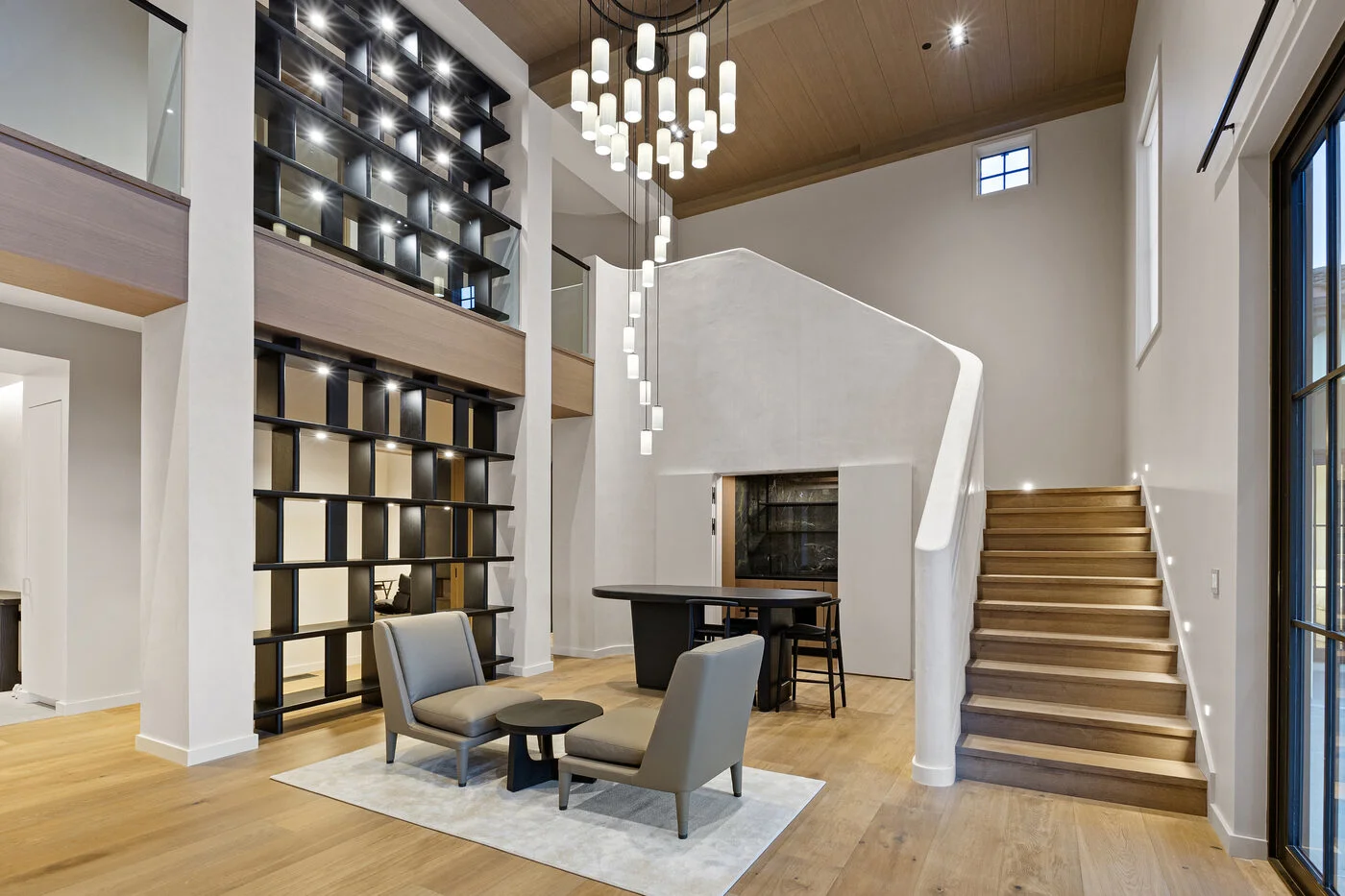 Grand double-height foyer with dramatic sculptural staircase, floor-to-ceiling backlit shelving and statement chandelier
