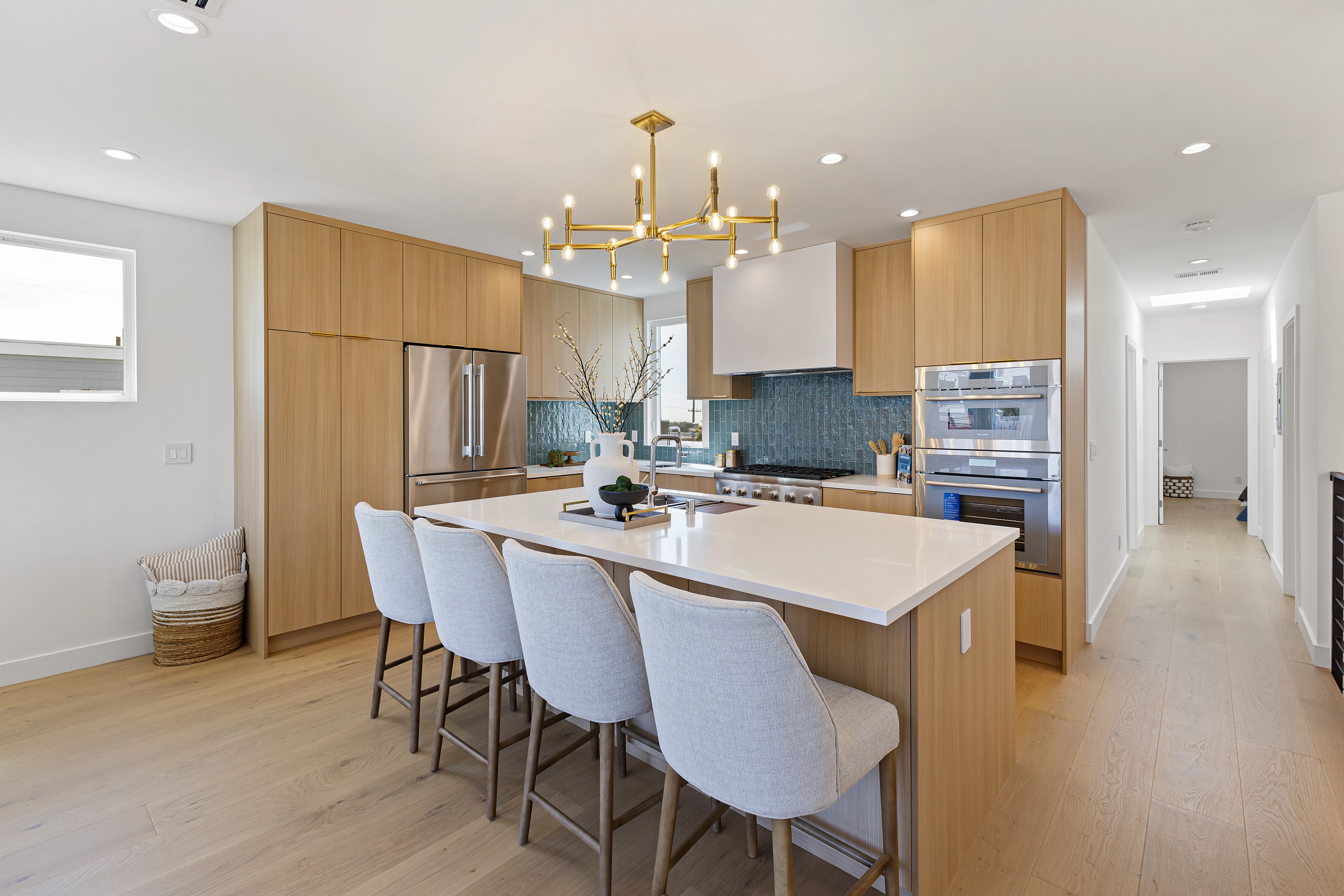 Bright kitchen with light oak cabinetry, teal zellige tile backsplash and gold sputnik chandelier