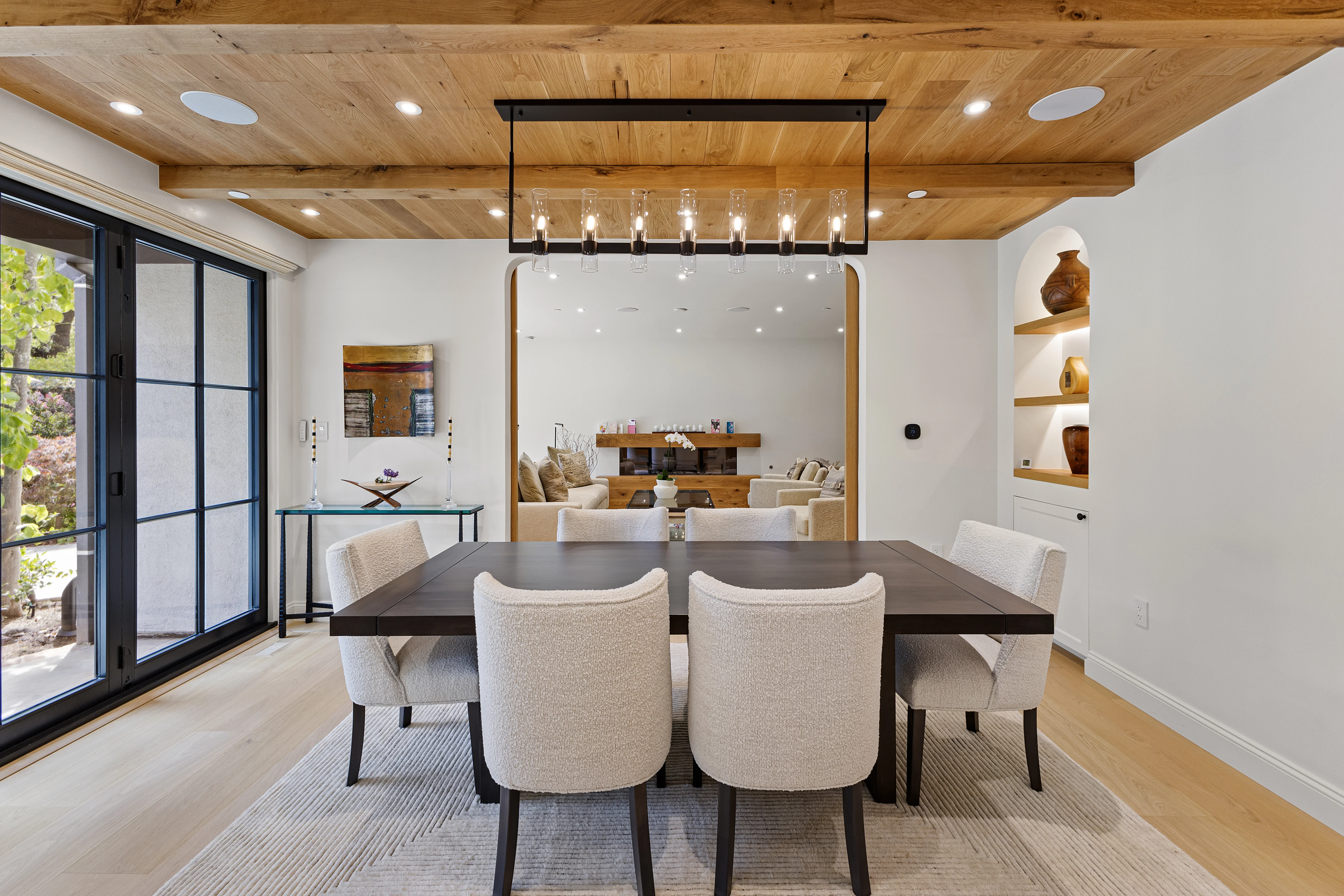 Warm dining room with natural wood plank ceiling, arched pass-through, and boucle upholstered chairs