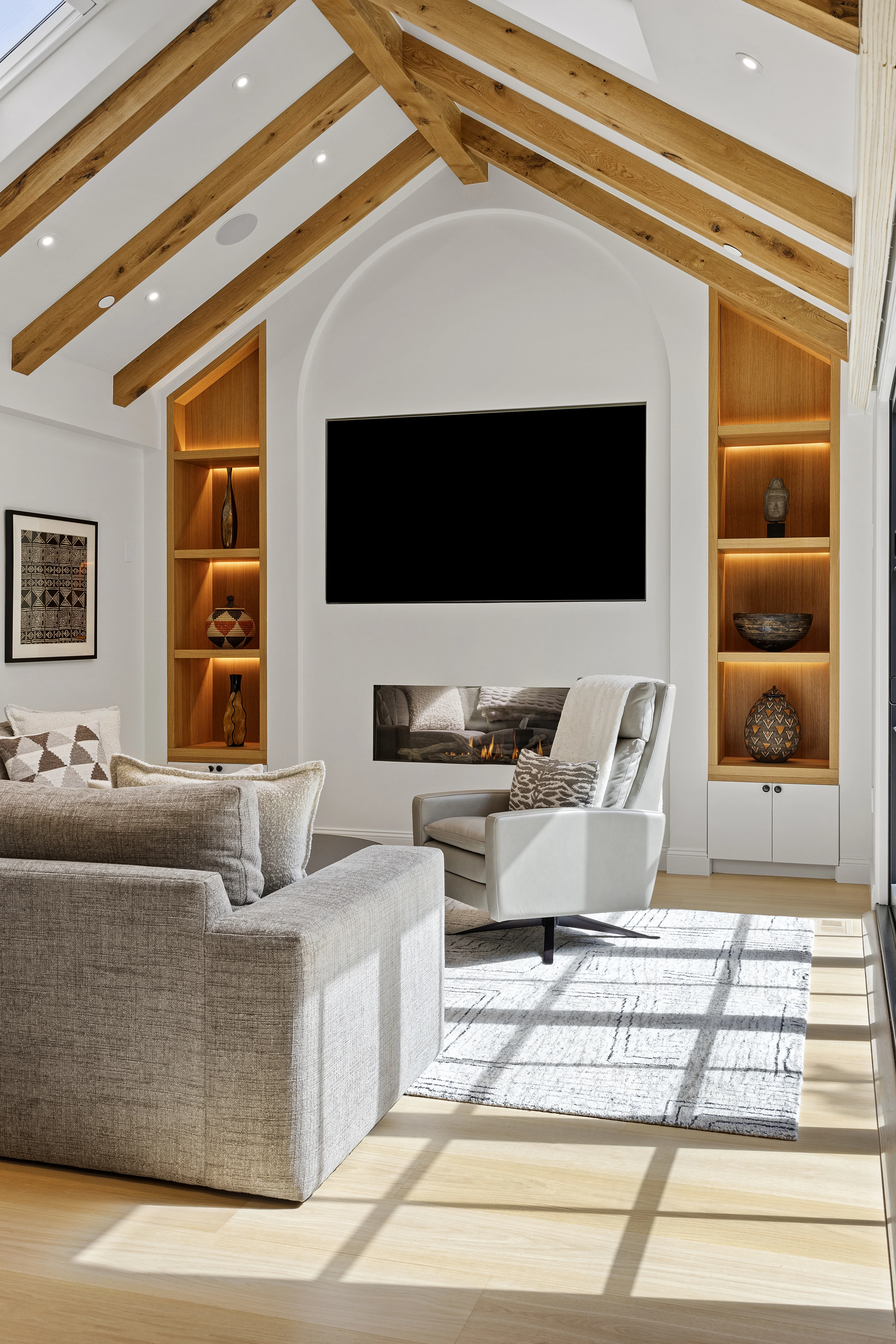 Living room with vaulted ceiling, exposed wood beams, arched fireplace niche and skylight flooding the space with natural light
