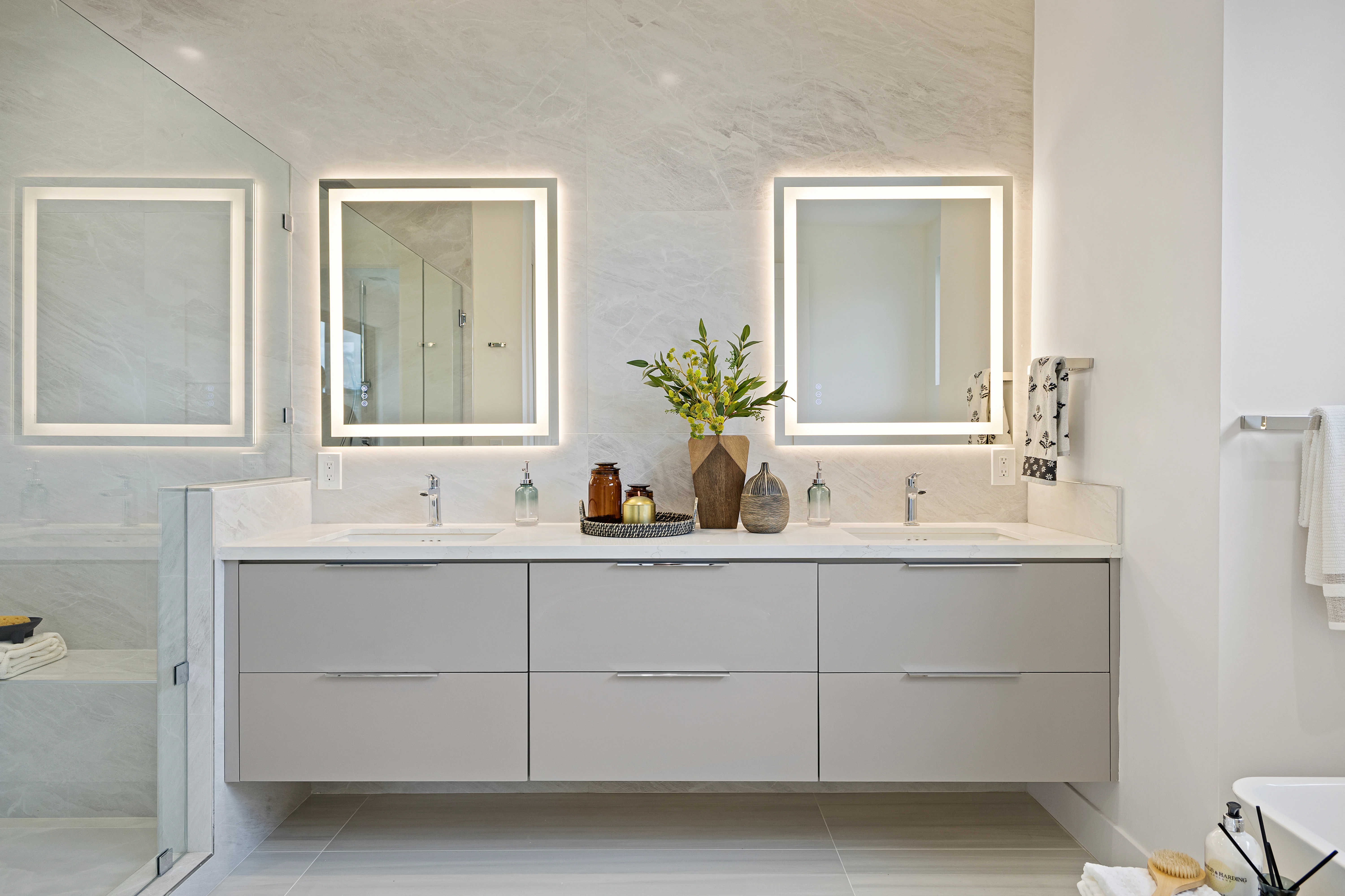 Spa-like master bathroom with double floating vanity, illuminated mirrors and full-height marble wall
