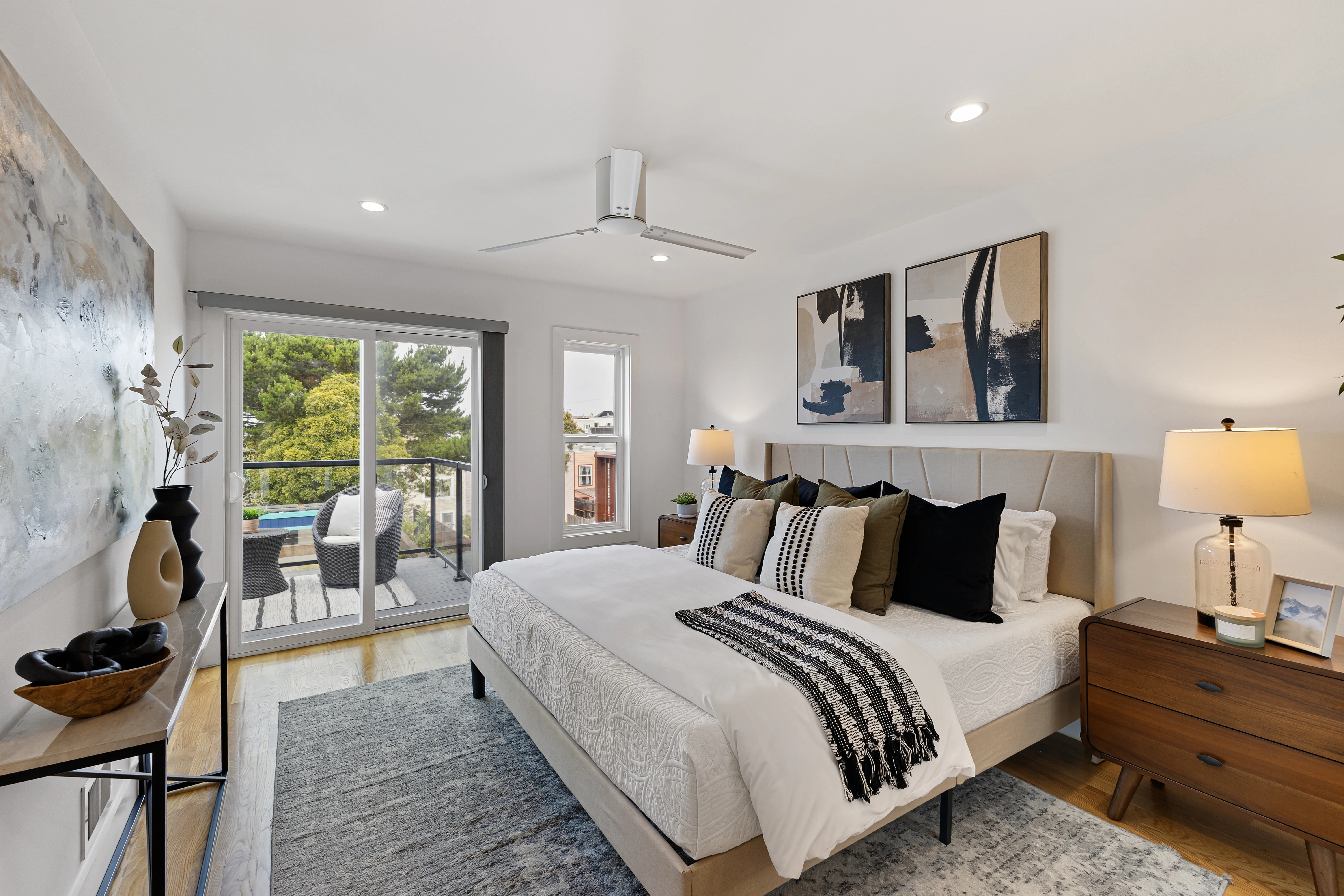 Primary bedroom with king bed, balcony access, abstract wall art and warm wood furniture